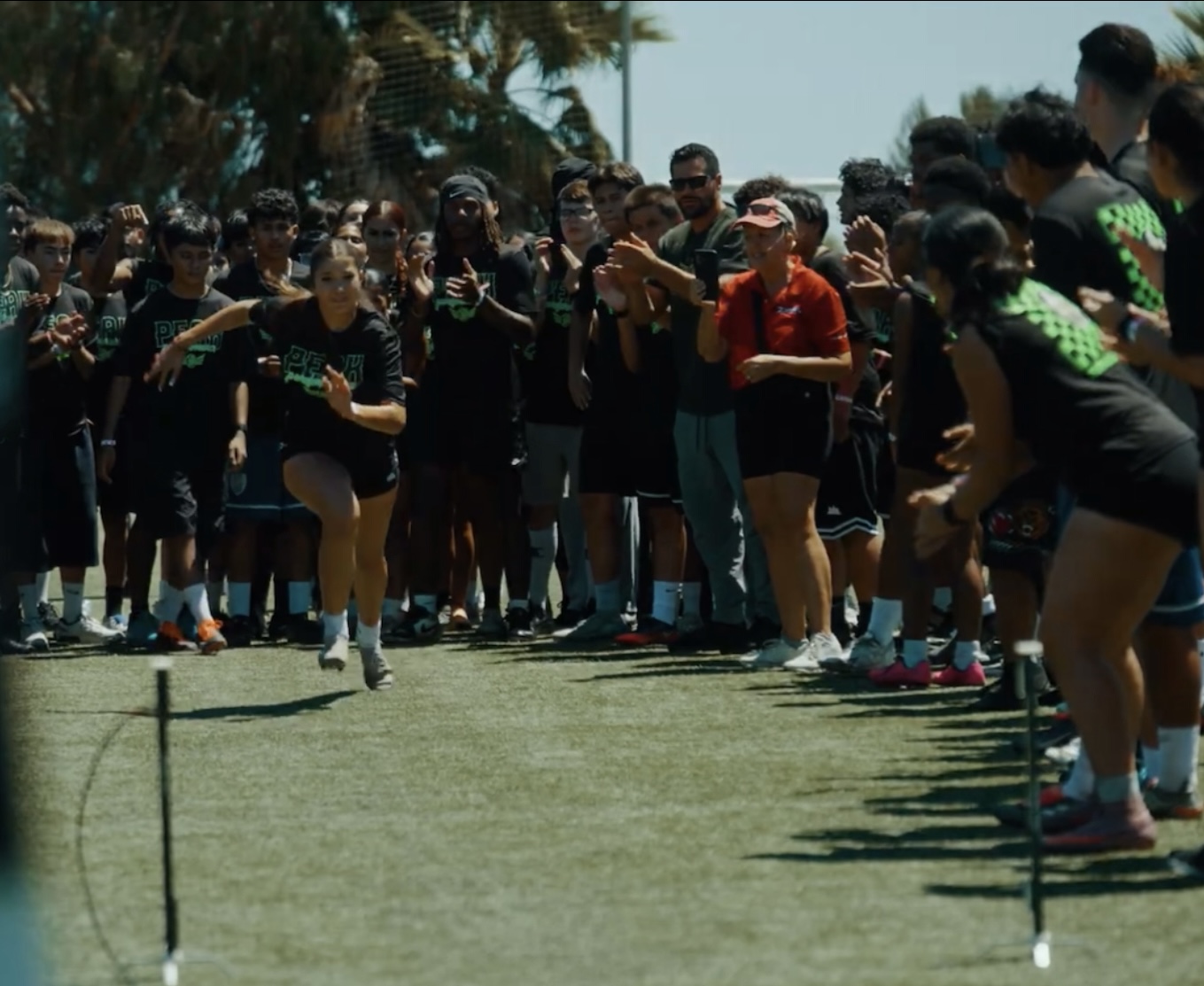 Young athlete accelerating in a field testing lane with peers cheering on either side